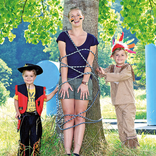 Kinder spielen Cowboy und Indianer mit einer Studentin.