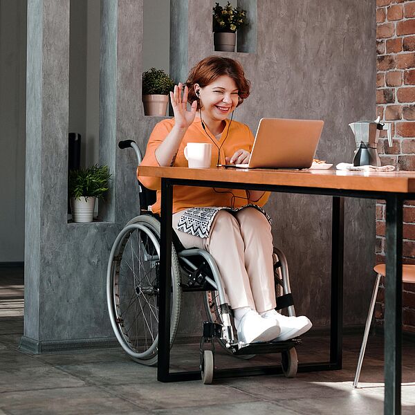 Young woman in a wheelchair participating in a video conference on her laptop in a café.